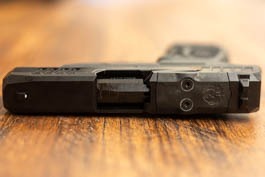 The black slide of a Ruger Max 9 from above with white dot sights on a tan wood background.